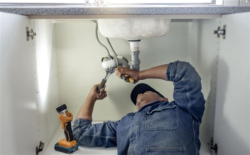 Plumber repairing pipes beneath a bathroom sink in Sunnyvale